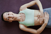 Top view of smiling woman doing yoga and lying on floor with hands on stomach