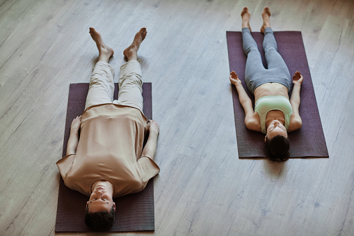 Top view at two young people lying down on floor in meditation with eyes closed, copy space