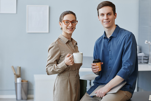 Portrait of two young business people man and woman looking at camera in office holding coffee cups during break, copy space
