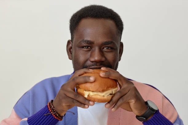 istock Young black man eating takeout burger and looking at camera against white 1499256675