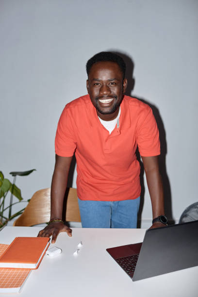 Smiling black man looking at camera at workplace and leaning on desk