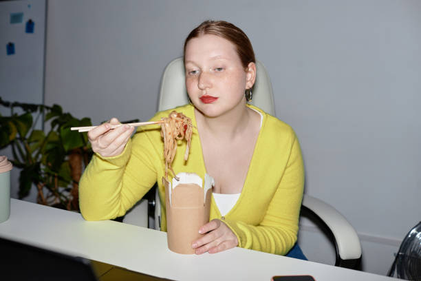 young woman eating takeout noodles indoors - coffee to go flash imagens e fotografias de stock