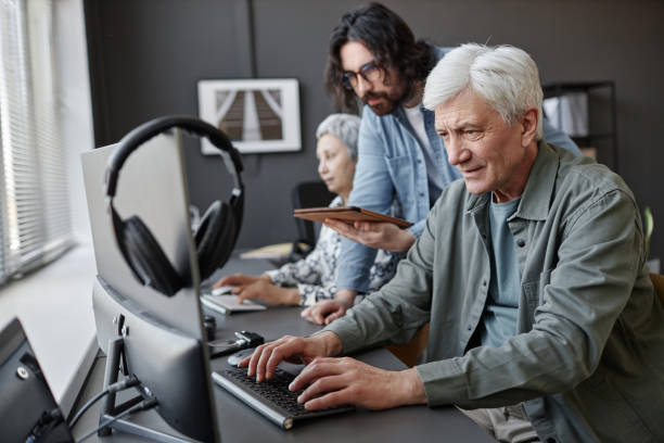 Senior man using computer in class with male instructor helping Side view portrait of senior man using computer in class with male instructor helping, copy space older software engineer stock pictures, royalty-free photos & images