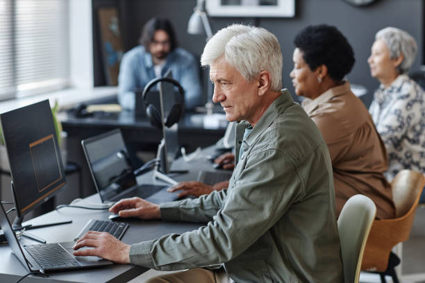 White haired man using computer in programming class for seniors Side view portrait of white haired man using computer in programming class for seniors older software engineer stock pictures, royalty-free photos & images