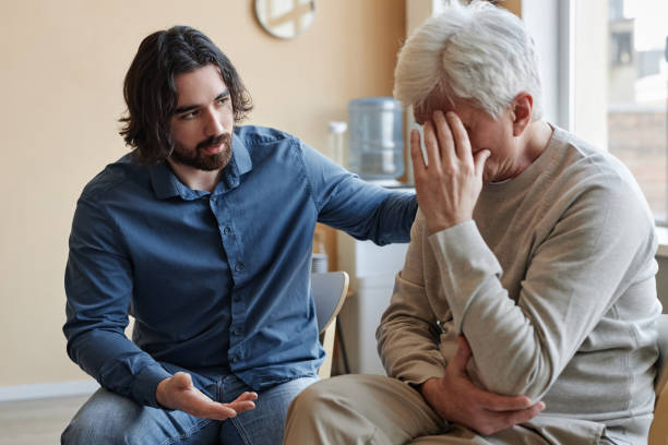 Male psychologist comforting senior man crying in mental health support group