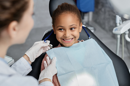 Niña sonriente en el sillón dental con una enfermera preparándola para el chequeo dental photo