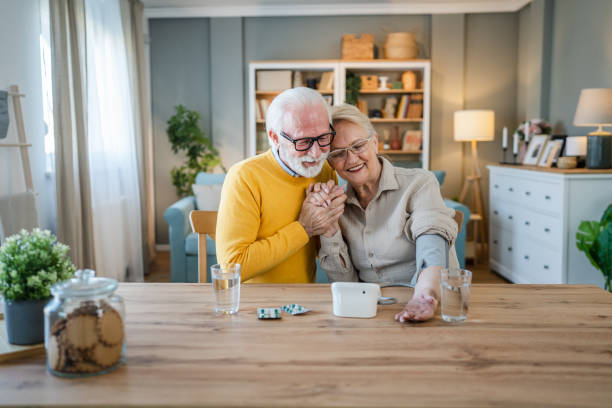 senior couple at home woman check blood pressure husband sit beside stock photo