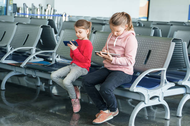 niños, niños, niñas esperando el vuelo del avión en la sala de salidas. sentado en sillas, jugando juegos de computadora en gadgets, teléfono móvil, tableta. chatea en redes sociales, video de wathing. estudia en línea - snowboarding snowboard teenager red fotografías e imágenes de stock