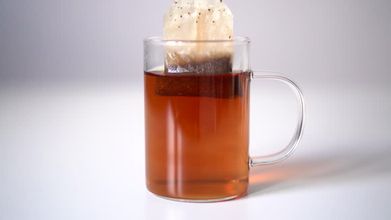 A tea bag of black English tea is brewed in a transparent glass mug on a white background, the morning tradition of making tea. Hot delicious drinks. Video 4K.