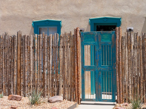 Rough post fence and aquamarine doorway against adobe wall in old town Albuquerque.