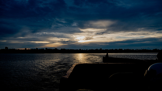the sun is setting over a body of water, taken with fujifilm xs10, archival pigment print, a man sitting on a jetty