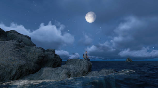 istock Man sitting on sea rocks under gloomy moonlight atmosphere. 1499294637