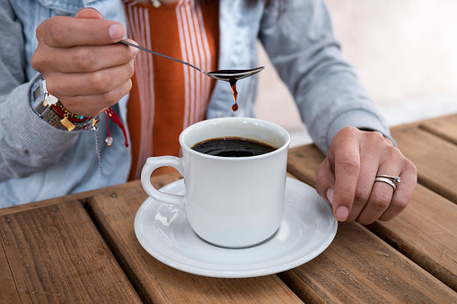 close up detail of woman's hands cooling a cup of coffee with the spoon on a wooden table