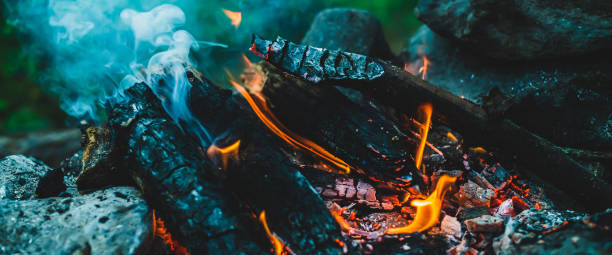 istock Vivid smoldered firewoods burned in fire close-up. Atmospheric warm background with orange flame of campfire and blue smoke. Unimaginable full frame image of bonfire. Burning logs in beautiful fire. 1499309326