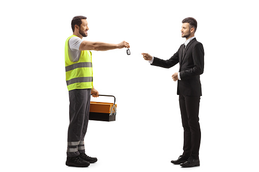 Full length profile shot of a road assistance agent giving car keys to a young businessman isolated on white background