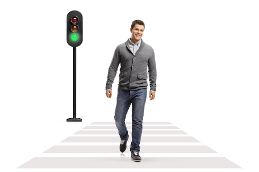 Full length portrait of a young smiling man walking at a pedestrian crossing isolated on white background