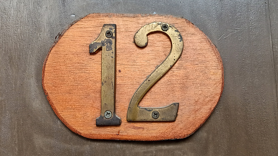 Close up old house number with engraving on wooden board, number 12 room sign. Door wooden brown color