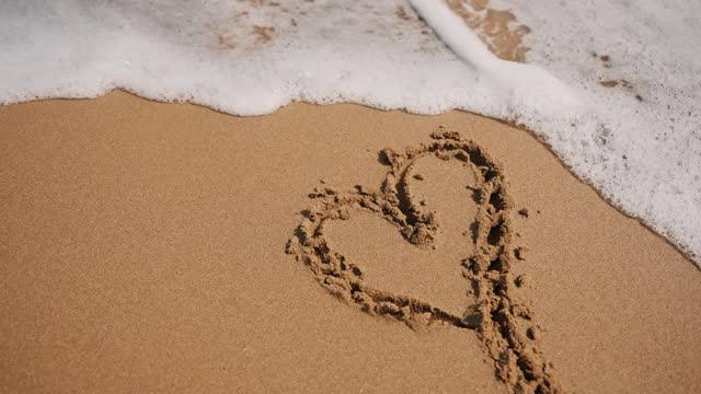 Reversed Clip Heart Drawn on Sand and Sea Foam on Shore at Beach