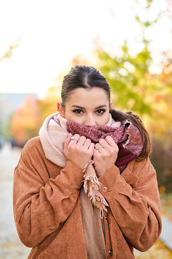 Caucasian young woman warming up her neck with a scarf during a cold autumn.