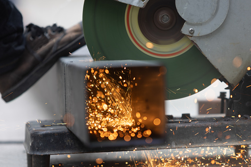 Worker cutting steel rectangular pipe in construction site.