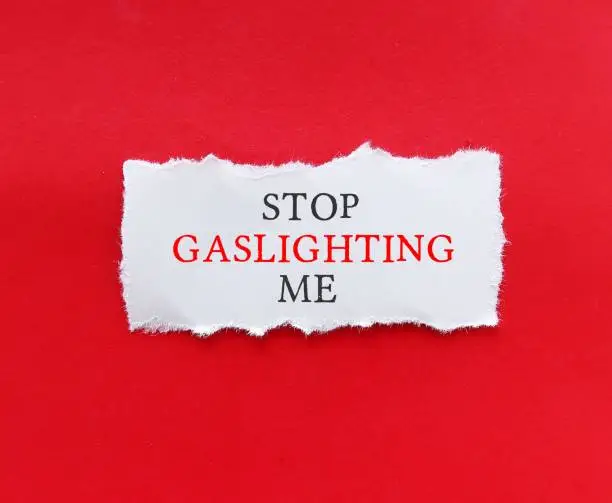 Torn note on red background with text STOP GASLIGHTING ME, to stop gaslighter, abuser who tries to control victim by twisting their sense of reality - manipulation in abusive relationships