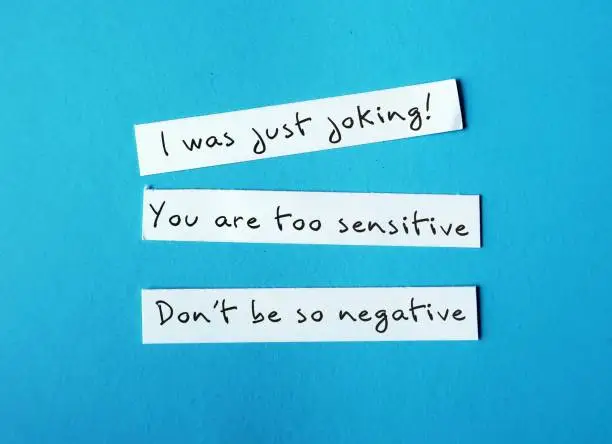 On blue background, torn paper with handwriting I WAS JUST JOKING, YOU'RE SO SENSITIVE and DON'T BE SO NEGATIVE, gaslighting verbal abuse use to manipulate and pin whole blame to victim