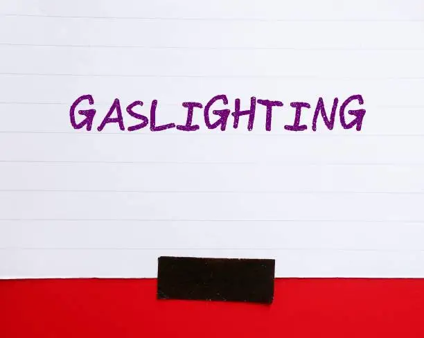 Note paper stick on red wall with handwriting text GASLIGHTING, refer to person who presents a false narrative to another which leads them to doubt their perceptions and become distressed and dependent on the gaslighter