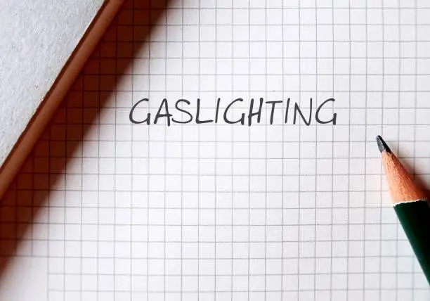 Pencil writing on note paper GASLIGHTING, refer to person who presents a false narrative to another which leads them to doubt their perceptions and become disoriented and dependent on the gaslighter