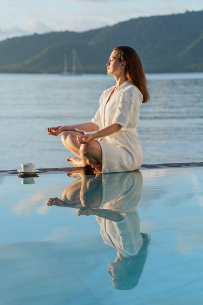 istock brunette in white robe sits at edge of pool, holding coffee mug 1499366638