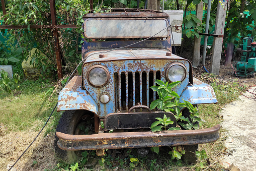 A rustic vintage abandoned car is left in a neglected condition in the garden. Front view
