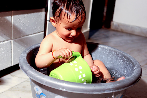 Baby child of Indian ethnicity taking a bath in bathtub at home with hot water during winter season video portrait indoor close up.