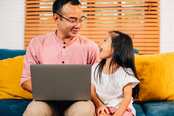 istock Father using laptop playing with daughter in living room 1499372109