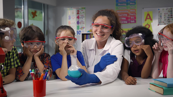 Female teacher and preschool children make experiment with chemicals in kindergarten. Multiethnic preschool kinds have science lesson in primary school