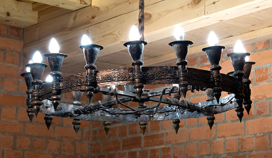Vintage large vintage chandelier with candle light bulbs hanging from a wooden ceiling. Metal openwork frame with forged ornament.