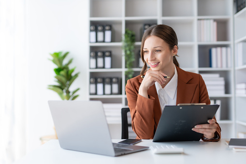 Beautiful young business woman manager or company worker holding accounting document, checking financial data or marketing report working in office with laptop. Accountant consults on some document.