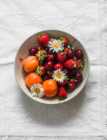 Seasonal summer berries and fruits - apricots, strawberries, cherries in a bowl on a light background, top view