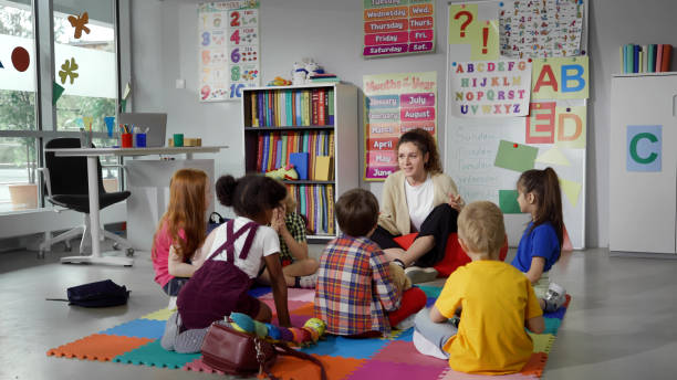 Small nursery school children with teacher sitting on floor having lesson Small nursery school children with teacher sitting on floor having lesson. Young woman teach preschool kids in classroom sitting on floor together preschool classroom stock pictures, royalty-free photos & images