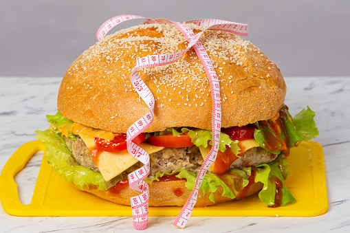 Hamburger wrapped in a measuring tape on a gray background. Weight loss concept.