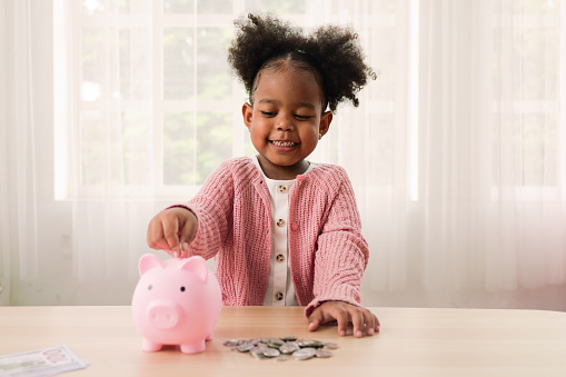 Little girl putting coin of cash into ceramic piggy bank, Happy daughter saving money for future into piggy bank
