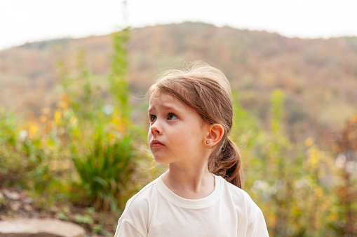 Portrait of a cute little girl in a white T-shirt against the background of autumn nature.