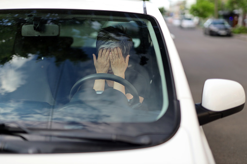 Frustrated woman covers her face with her hands in the driver's seat.