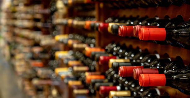 bottles of black red wine lined up and stacked on wooden wine rack shelves from a private collection of a wine cellar in spain. - wine cellar liquor store wine rack imagens e fotografias de stock