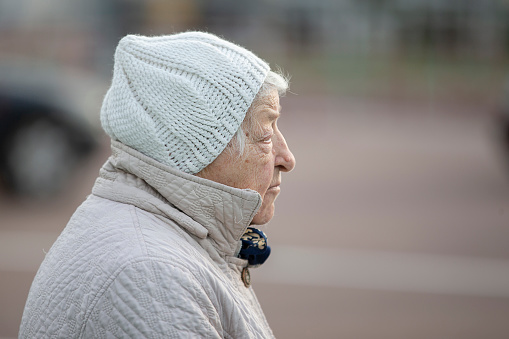 The face of an elderly woman in a profile in warm clothes. A sad pensioner in gray clothes.