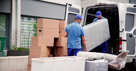 Male Workers In Blue Uniform Unloading Furniture From Truck