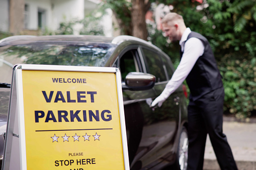 Man Giving Car Key To Male Valet Near Valet Parking Sign