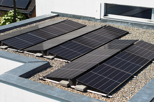 New Solar Panels - Photovoltaic System installed on top of flat roof on modern Private Home - Sustainable Green Building. Aerial Drone Point of View. Carbon Footprint - Green Energy - Sustainable Energy at in modern Homes Concept. Southern Germany, Europe