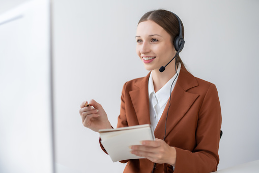 Call center agent woman with headset working on support hotline in modern office. Smiling female customer support phone operator at workplace.