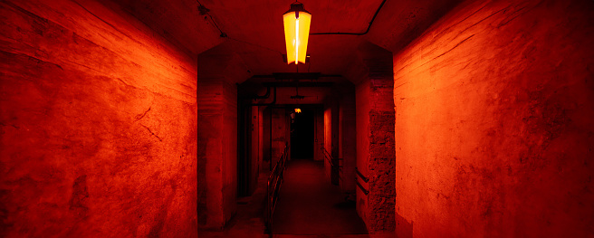 Granite and cement tunnel or bunker passages in the underground illuminated with dramatic red light of florescents with walkways with many dark corridors to hold prisoners or hide from war