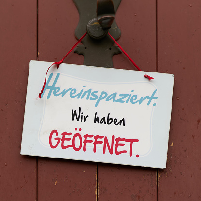 Sign on an entrance door with the German inscription Hereinspaziert wir haben geöffnet. Translation: Come in we are open