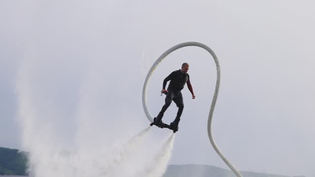 Flyboarding is a new extreme sport where a joyful male flyboarder flies over the water and performs tricks, creating a spectacular display of activity on the water